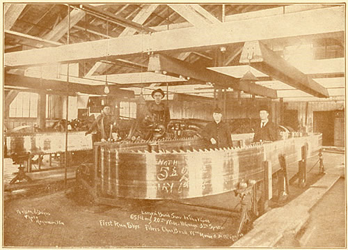 Photo of a filing shop with a band saw ready to be filed, four men pose with the saw, ca. 1918.